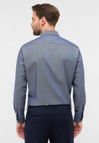 Camicia da uomo con un motivo a spina di pesce blu chiaro e blu scuro, maniche lunghe con polsini abbottonati e colletto classico, vista da dietro.