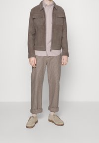 Ruskea samettitakki, jossa on kaksi rintataskua, vaalea ruutupaita, kuvioidut housut ja vaaleat kiiltonahkakengät paksulla pohjalla.