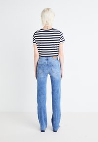 Camisa de rayas de manga corta con cuello redondo, combinada con jeans de mezclilla rectos de color azul claro que tienen bolsillos traseros y un lavado deslavado.