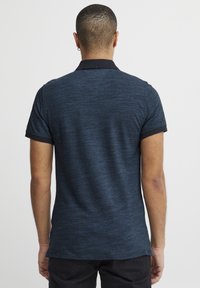 Marineblaues Polohemd, kurze Ärmel, strukturierter Stoff, kontrastierender dunkler Kragen, schmaler Schnitt und seitliche Schlitzsäume für mehr Bewegungsfreiheit.