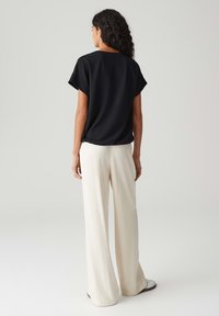 Zwart textuurtop met korte mouwen, gecombineerd met losse witte broek. De outfit heeft een relaxte pasvorm en een minimalistisch ontwerp.