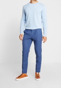 Light blue crew-neck sweater, fitted blue pinstriped trousers, and brown leather sneakers with white soles. Casual, tailored look.
