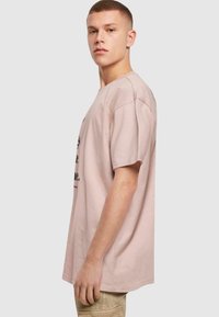 Lys pink bomulds t-shirt med korte ærmer og afslappet pasform, med sort tekst på fronten. Enkel design og glat tekstur.
