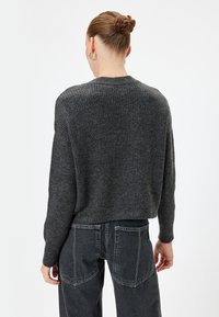 Pull en maille côtelée gris foncé avec un col rond et des épaules tombantes, associé à un jean noir taille haute avec des poches à rabat distinctives.