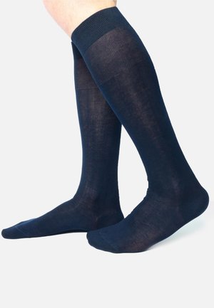 Calze al ginocchio di un blu navale scuro, realizzate in un tessuto leggero e morbido con una fascia a coste nella parte superiore e una punta senza cuciture. Superficie testurizzata con una leggera lucentezza.