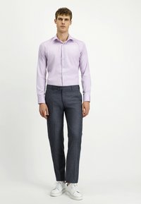 Camicia dress leggera di colore viola chiaro con bottoni, abbinata a pantaloni grigi scuri con trama e sneakers bianche. Design slim-fit, maniche lunghe visibili.