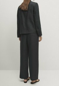Black linen blazer with a relaxed fit, paired with wide-leg trousers. Smooth texture, minimal design, and worn with flat sandals.