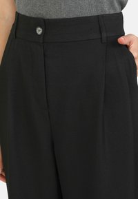 Black tailored trousers featuring a flat front, side pockets, and a single button closure. The fabric has a smooth, matte texture.