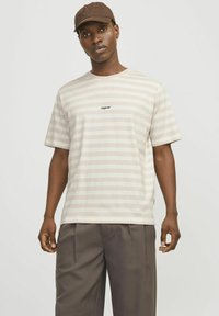 Camiseta a rayas en beige claro y crema, hecha de algodón suave. Presenta mangas cortas y un pequeño logo de "Originals" en el pecho.