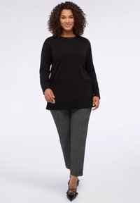 Černý dlouhý svetr s vroubkovaným lemem, kombinovaný se šedými pruhovanými kalhotami s manžetami u kotníků a černými lodičkami s hrotitými detaily.