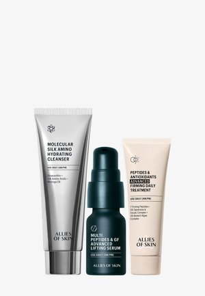 Drei Hautpflegeprodukte: eine silberne Tube, eine dunkelgrüne Pumpflasche und eine hellbeige Tube, die jeweils mit Produktnamen und Anwendungshinweisen gekennzeichnet sind.