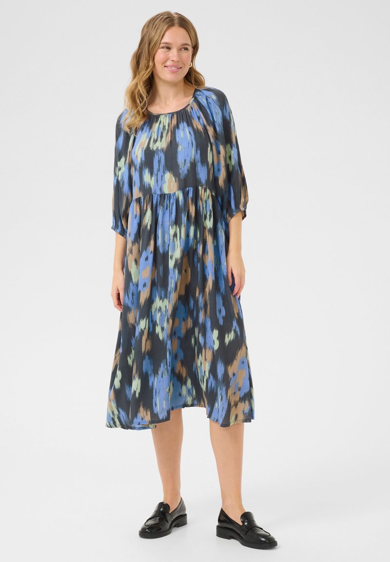 Un vestido de longitud media, de corte suelto, con un patrón colorido en azul, verde y marrón. Presenta un escote fruncido y mangas de tres cuartos.
