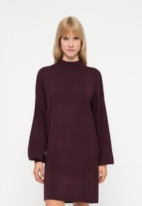 Abito lavorato a maglia bordeaux con collo alto, maniche lunghe oversize e vestibilità morbida, caratterizzato da una finitura liscia e testurizzata.