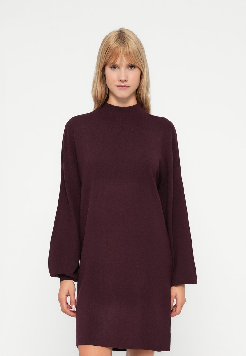 Abito lavorato a maglia bordeaux con collo alto, maniche lunghe oversize e vestibilità morbida, caratterizzato da una finitura liscia e testurizzata.