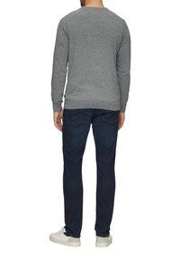 Szary dziergany sweter z okrągłym dekoltem i prążkowanym dołem, noszony z ciemnoniebieskimi dżinsami i białymi trampkami, widziany od tyłu.