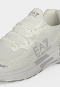 Λευκό sneaker EA7 Emporio Armani με πλεκτό επάνω μέρος, κορδόνια και λογότυπο της μάρκας στο πλάι και στη γλώσσα.