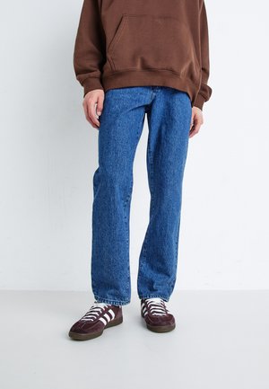 Blå jeans med rette ben, kombinert med en brun hettegenser og burgunder sneakers med hvite striper.