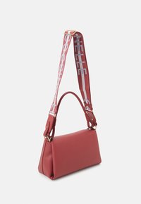 Czerwona torebka o teksturowanej powierzchni w prostokątnym kształcie, z dodatkami w kolorze złotym oraz wielokolorowym, regulowanym paskiem z napisem.