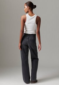 Crne traperice širokih nogavica s visokim strukom, s dva stražnja džepa i glatkom teksturom, uparene s uskim bijelim topom.