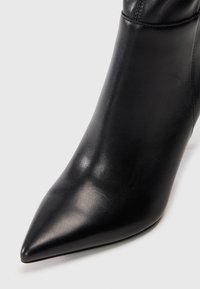 Schwarze Leder-High-Heel-Stiefel mit spitzem Zeh. Glatte Textur und elegantes Design, mit einem engen Schaft und minimaler Gestaltung.