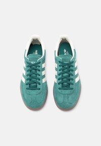 Semišové tenisky v tyrkysovej farbe s bielym dizajnom troch pruhov, okrúhlym špičkou a hnedou gumovou podrážkou s textúrou. Šnúrky v zodpovedajúcej tyrkysovej farbe.