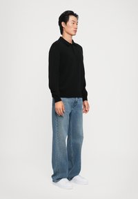 Polo shirt negru cu mânecă lungă și guler, asortat cu blugi largi albaștri și adidași albi. Design simplu, cu detalii minime.