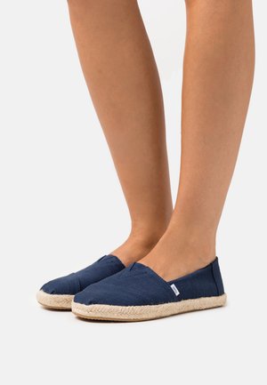 Navy canvas slip-on shoes with a round toe and woven jute sole. Simple design with a textured fabric upper and stitching detail along the seams.