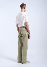 Ljusgröna vida jeans med sömnadsdetaljer och två bakfickor, matchat med en vit t-shirt och grå sneakers.