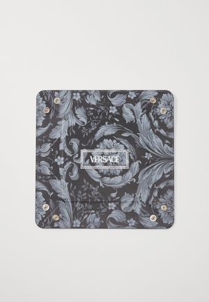 Tecido preto com padrão que apresenta desenhos florais e paisley em azul claro, com acessórios em prata e um rótulo branco "VERSACE" ao centro.