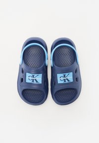 Sandali blu navy con una soletta testurizzata e aperture laterali. Presentano una fascia azzurro chiaro e un'etichetta con logo. Realizzati in materiale leggero e flessibile.