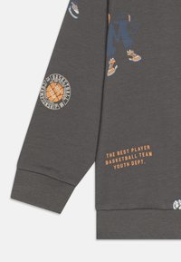 Szary sweatshirt z grafiką koszykówki i pomarańczowym napisem. Projekt zawiera prążkowane mankiety i nadrukowane akcenty na rękawach.