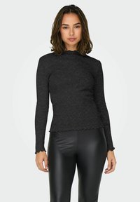 Top lungo a maniche nere a coste con scollatura e orli ondulati, caratterizzato da un design aderente e tessuto testurizzato. Abbinato a leggings neri.