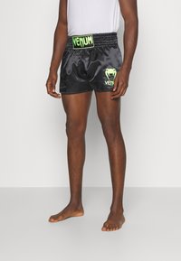 Calções de boxe em satin preto com um cós elástico, logo e detalhes em verde "VENUM", até ao joelho com um corte largo e ventilação lateral.
