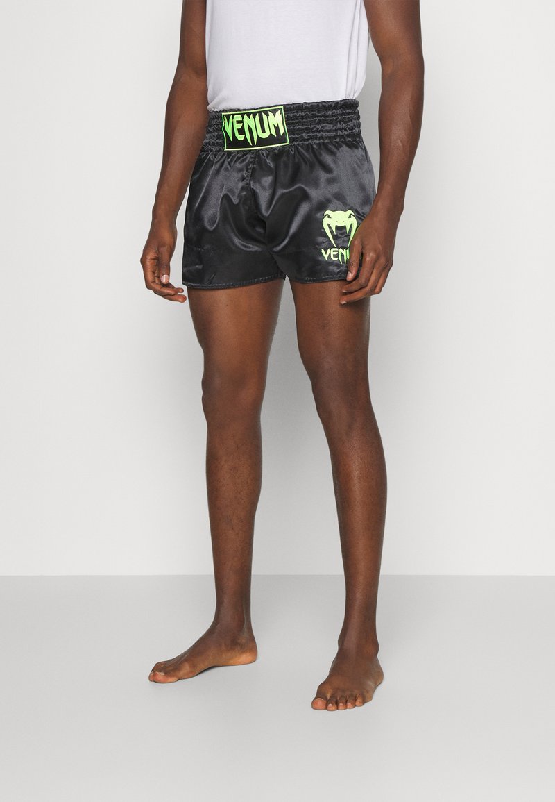 Calções de boxe em satin preto com um cós elástico, logo e detalhes em verde "VENUM", até ao joelho com um corte largo e ventilação lateral.