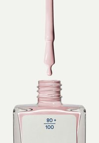 Flaska med ljusrosa nagellack i en klar glasbehållare och vit etikett som visar numeriska värden, med en pensel som droppar nagellack ovanför.