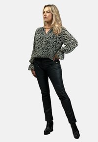 Czarna i biała bluzka w wzory z długimi rękawami, zestawiona z czarnymi skórzanymi spodniami typu slim oraz masywnymi czarnymi botkami na obcasie.