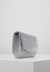 Srebrna wieczorowa torebka pokryta błyszczącymi kamieniami. Posiada zapięcie na klapkę oraz gładkie wykończenie wnętrza. Kompaktowy, prostokątny kształt z zaokrąglonymi krawędziami.