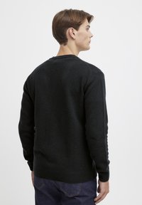Mørk strikkegenser med rund hals, med ribbestrikkede mansjetter og kant. Glatt tekstur, tettsittende design og lange ermer.