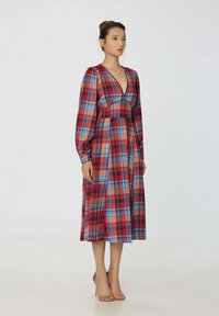 Robe midi à carreaux rouge et bleu avec des manches longues, décolleté en V profond et taille cintrée. Ce modèle présente un tissu fluide et une jupe plissée.