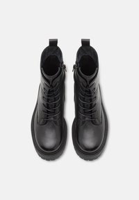 Botas de tobillo de cuero negro con punta redonda, cordones en la parte delantera y cremallera lateral. Presentan un interior texturizado y suela de goma para mayor agarre.
