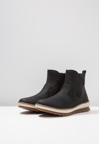 Svarta läderankle boots med en texturerad yta, elastiska sidopaneler och en beige gummisula med ett zigzag-mönster.