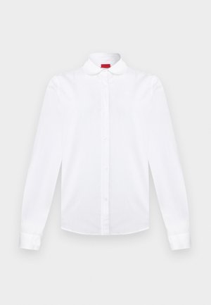 Hvit langermet skjorte med knapper, avrundet krage, knappet front og mansjetter, vist mot en ensfarget bakgrunn.