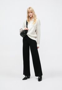 Oversized lichtgrijze trui met de tekst "Club", zwarte broek met wijde pijpen, zwarte handtas en zwarte enkellaarzen met puntige neus; gladde texturen.