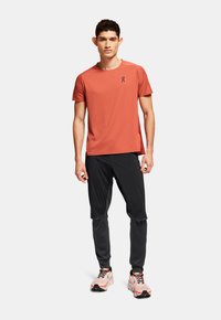 Herre atletisk outfit bestående af en åndbar rød T-shirt med korte ærmer og sorte tapered bukser, parret med pink løbesko og sorte accenter.