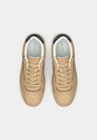 Μπεζ σουέτ αθλητικά παπούτσια με καφέ κορδόνια και αντίθετες ναυτικές λεπτομέρειες, διαθέτοντας τρυπητές λεπτομέρειες και στρογγυλό σχέδιο στη μύτη.