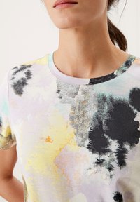 T-shirt en coton avec un col rond, des manches courtes et un motif abstrait multicolore aux teintes de jaune, noir et pastels.
