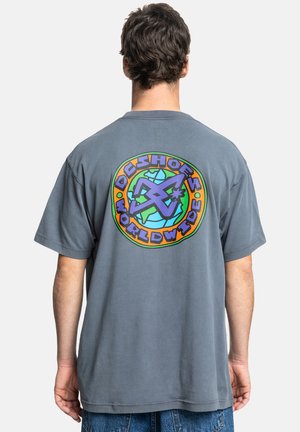 Graues Baumwoll-T-Shirt mit kurzen Ärmeln, das auf der Rückseite ein farbenfrohes, rundes Logo mit dem Text "DC Shoes Worldwide" zeigt.