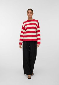 Maglione a righe rosse e bianche con vestibilità comoda, maniche lunghe e collo a girocollo a costine, abbinato a pantaloni larghi neri e sandali.