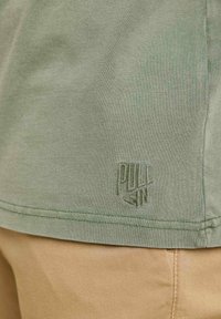 T-shirt en coton vert khaki à manches courtes, avec un logo brodé texturé au bas de l'ourlet et de petites coutures latérales.