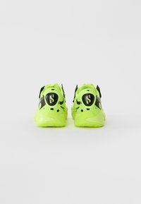 Lyse neon grønne atletiske sko med sorte detaljer og et stiliseret "S" logo på hælen, vist fra bagsiden på en hvid baggrund.